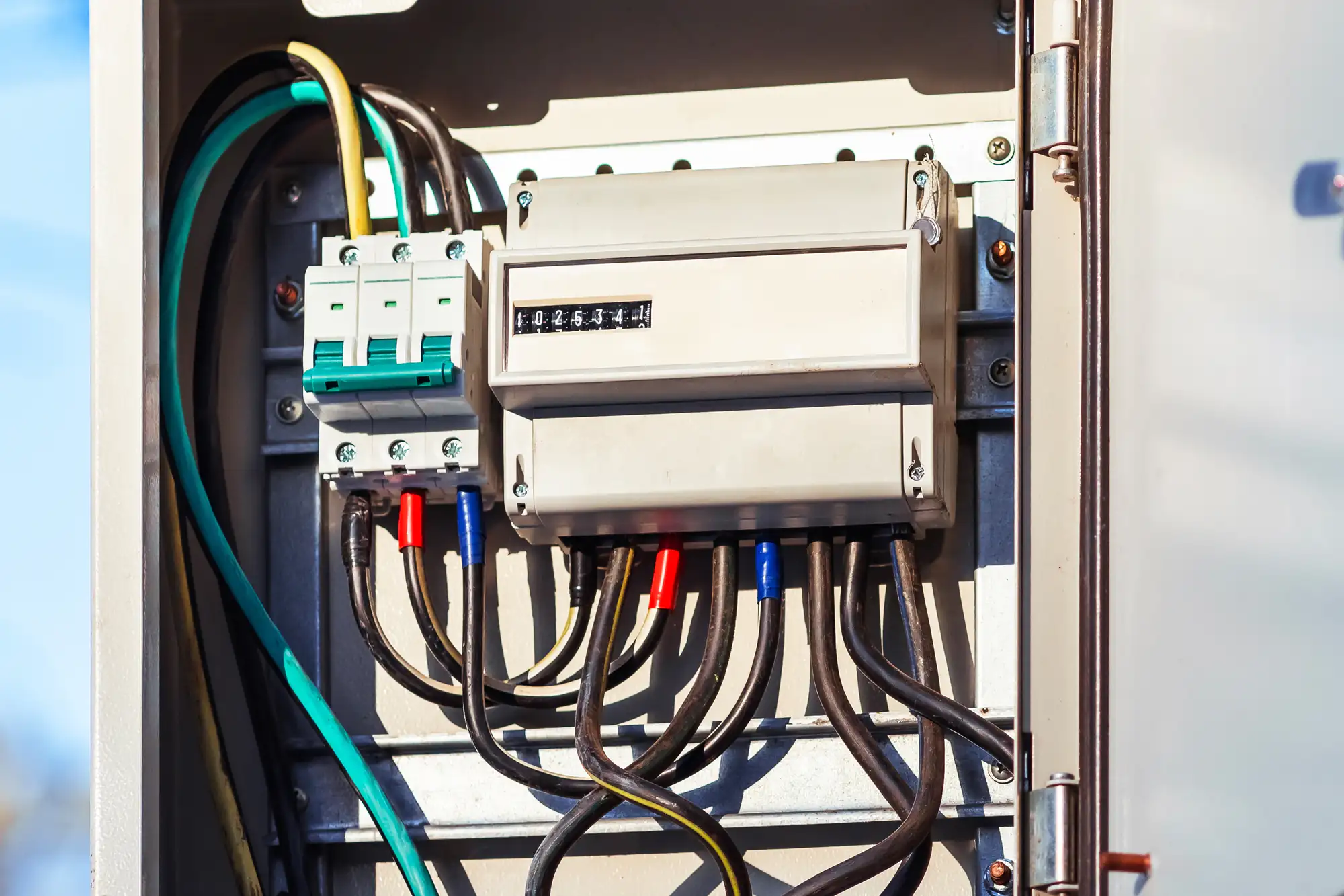 An open electrical panel in Brooklyn, NY shows multiple black wires connected to terminal blocks and a meter inside a gray box, with colored wire insulation and circuit breakers&mdash;ready for an electrician&rsquo;s expert touch.