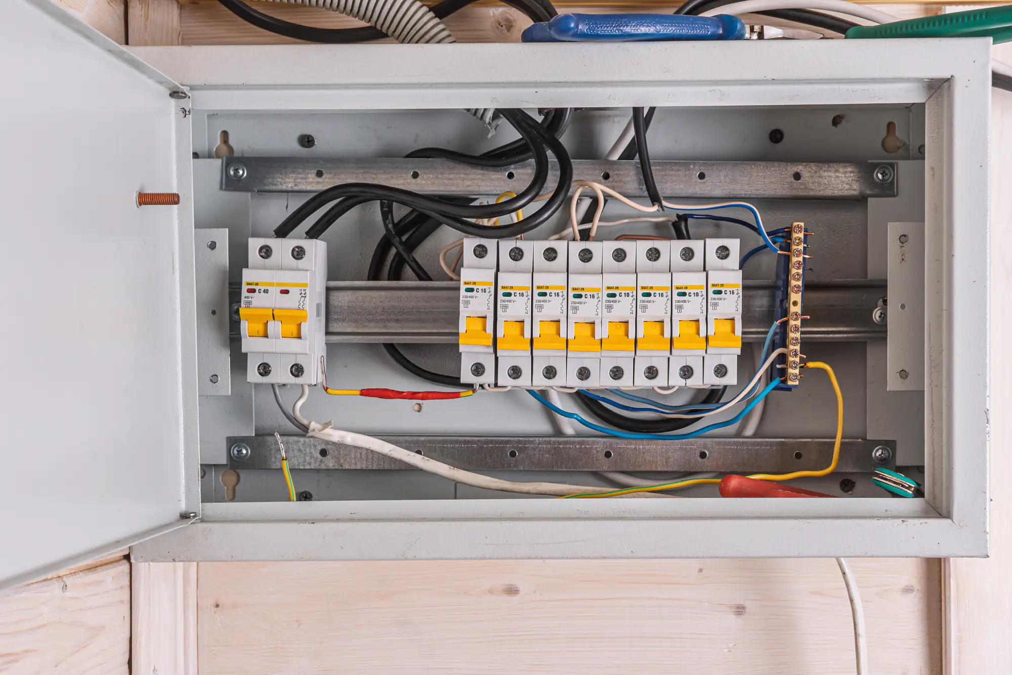 An open electrical panel with multiple circuit breakers, wires, and switches inside a metal box mounted on a light-colored wall, as serviced by an experienced electrician in Brooklyn, NY. The breakers have yellow switches and various colored wires are connected.
