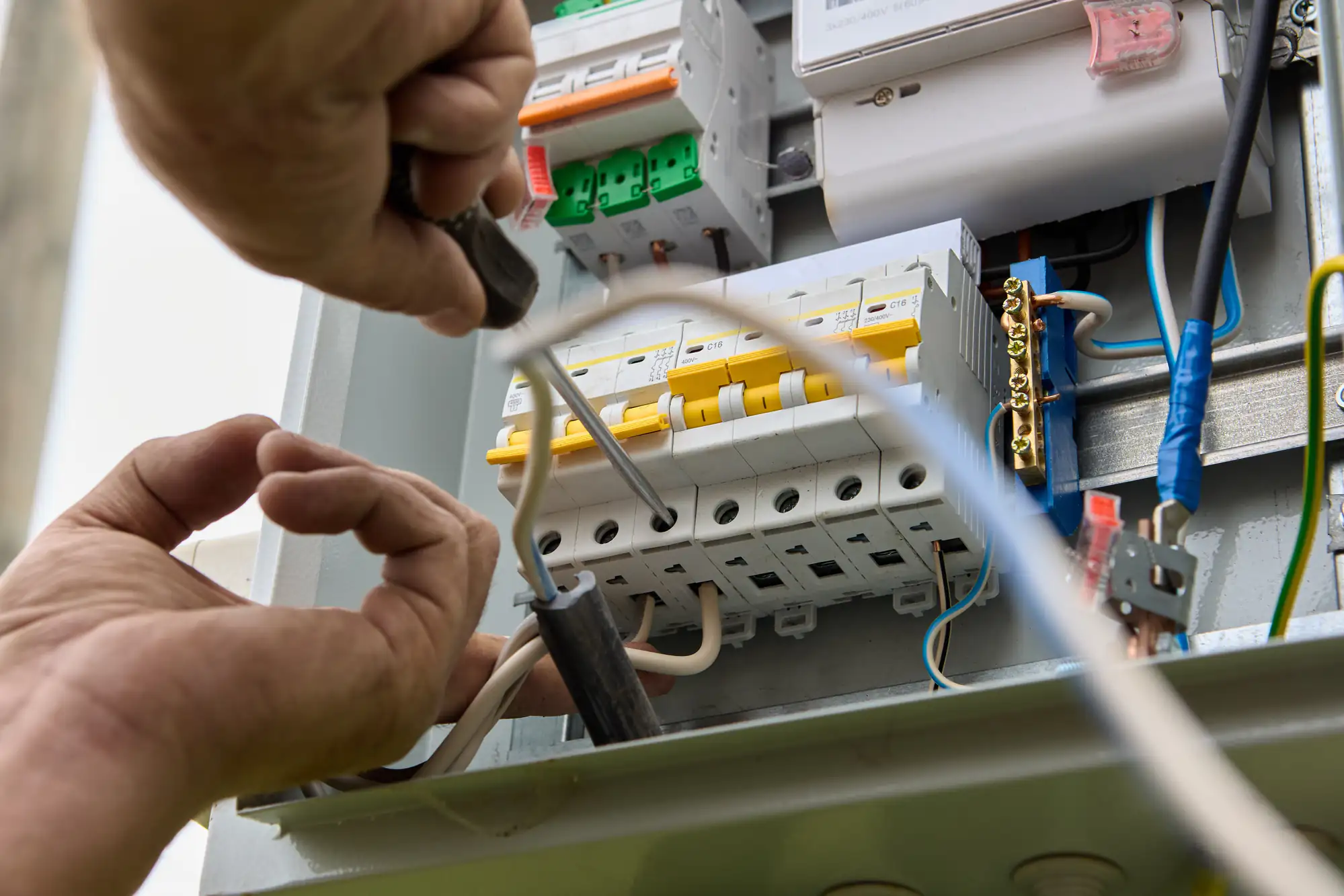 Close-up of an electrician in Brooklyn, NY using a screwdriver to work on wiring inside an electrical panel, with circuit breakers and various colored wires visible.