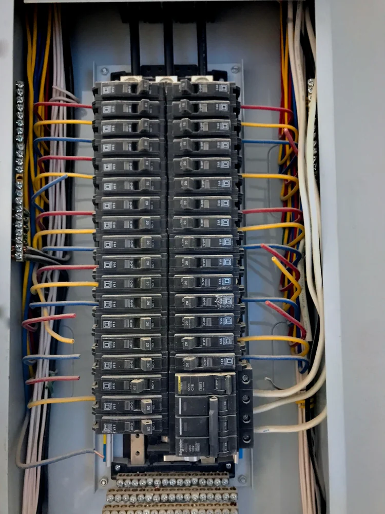 An electrical breaker panel with multiple circuit breakers, various colored wires connected to each breaker, and neatly organized wiring along the sides of the metal enclosure.