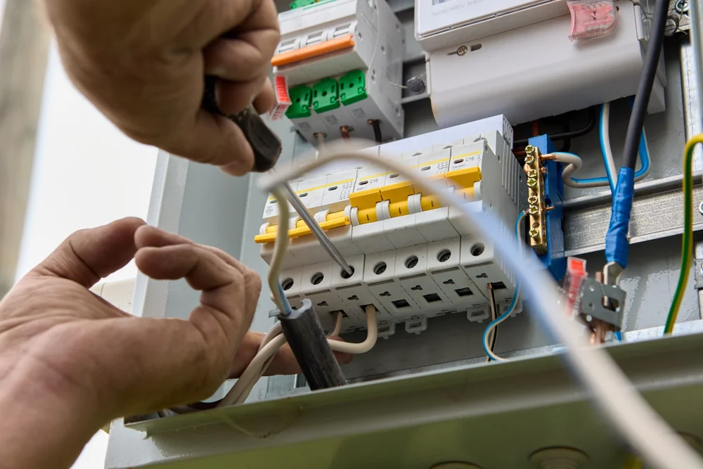 Close-up of a person&rsquo;s hands working on an electrical panel, using a screwdriver to connect wires to circuit breakers inside the control box.