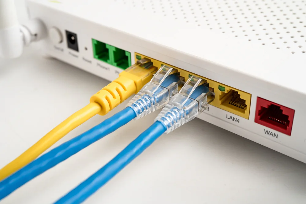 Close-up of a white Wi-Fi router with three network cables plugged into LAN ports and one cable in the WAN port. The router also shows power and other connection ports.